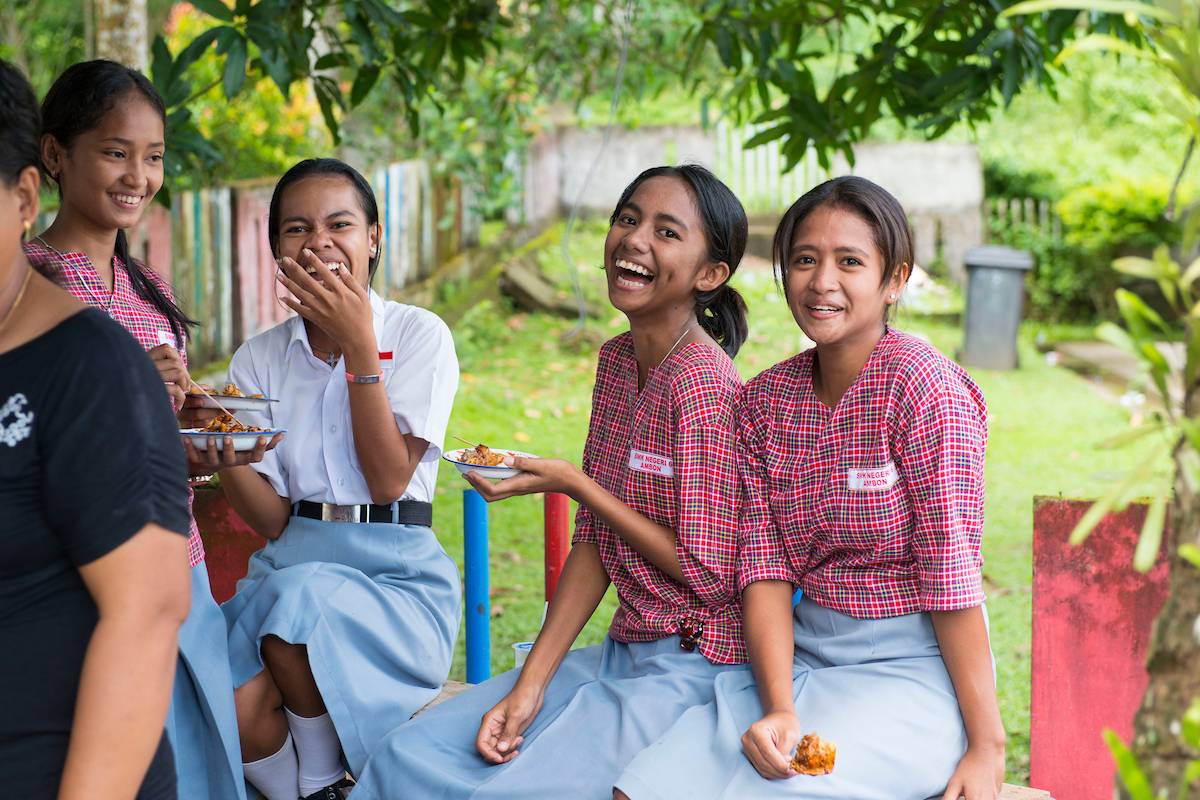 Four teen girls from Indonesia smiling and laughing while eating food.